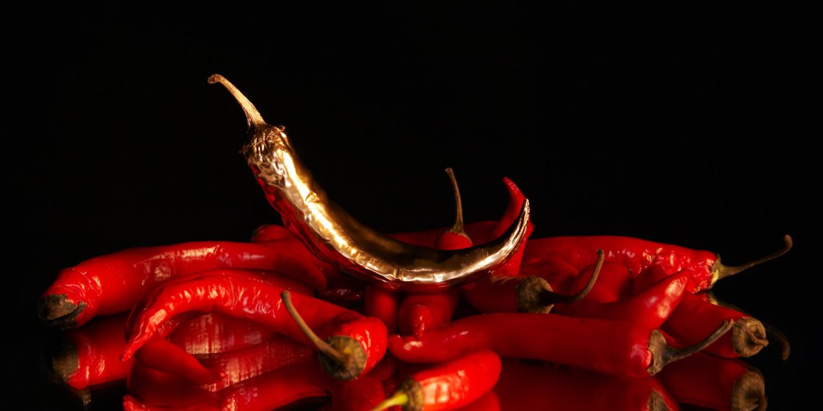 Conceptual composition: a golden chilli pepper stands on a red chilli pappers which lies on a mirror